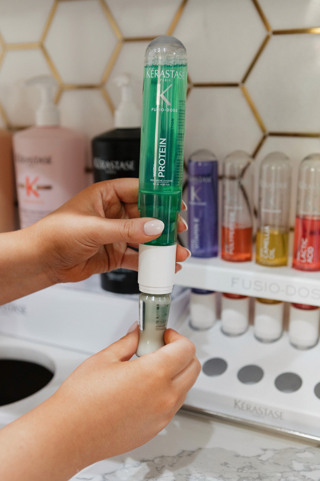 A smiling woman with her arms crossed, standing against a dark green background. She has long, dark hair.