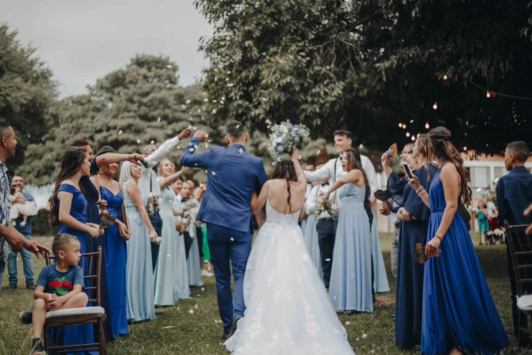Bride and groom walking through a confetti toss from bridesmaids in blue dresses at an outdoor garden celebration