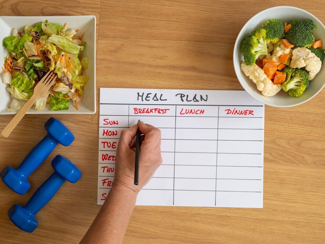 closeup of a person writing out a meal plan on a handmade table to support their resistance training for weight loss