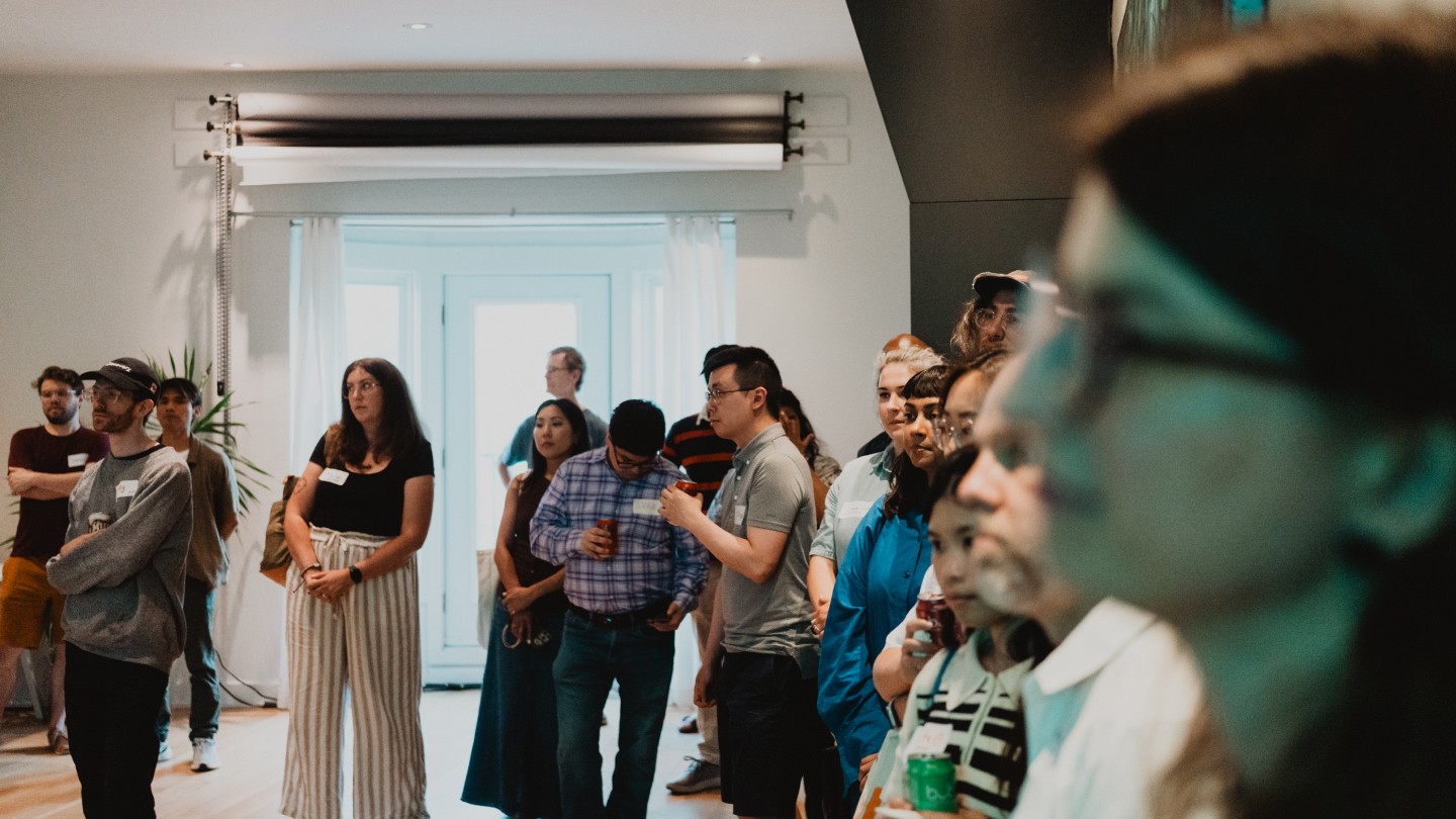 A diverse group of people attentively listen to a presentation in a bright room. They appear focused and engaged, creating a thoughtful atmosphere.