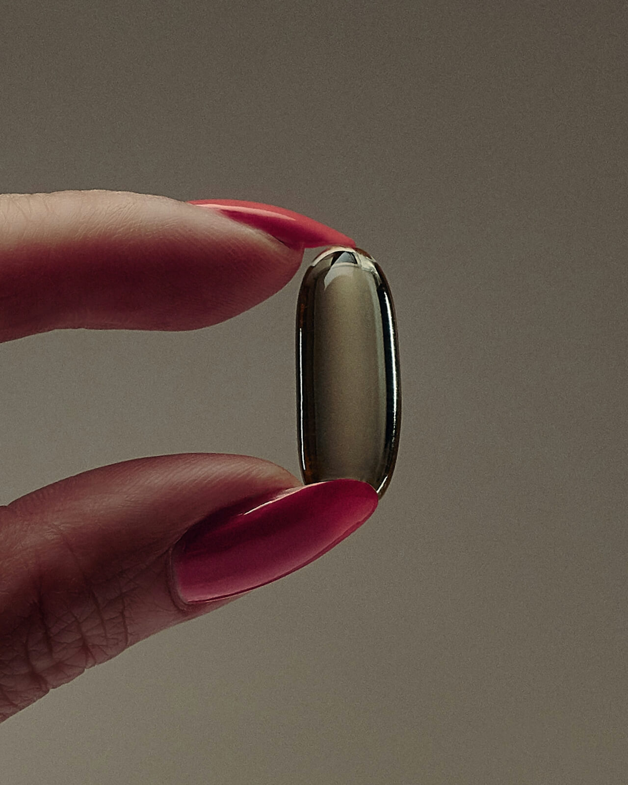 Close up of a capsule supplement being held between a lady's manicured index finger and thumb