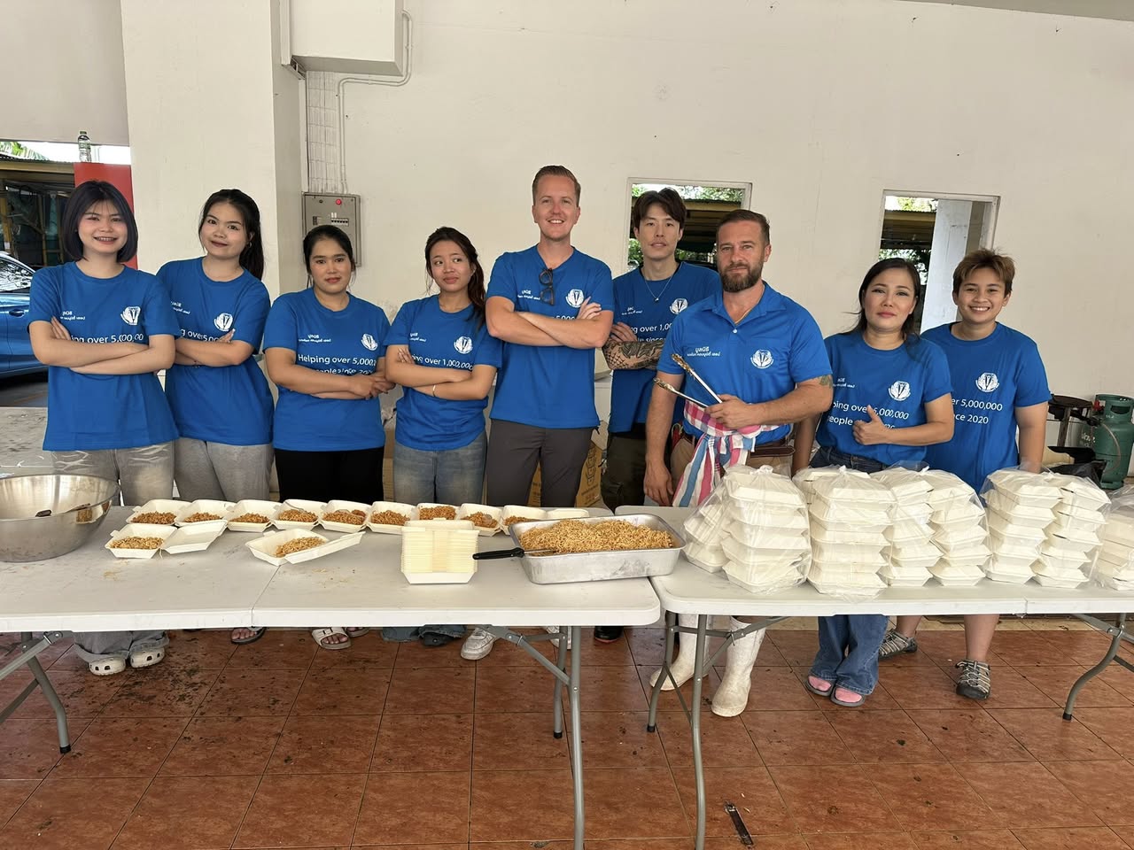man in blue t-shirt and white floral skirt holding black smartphone while sitting on sidewalk
