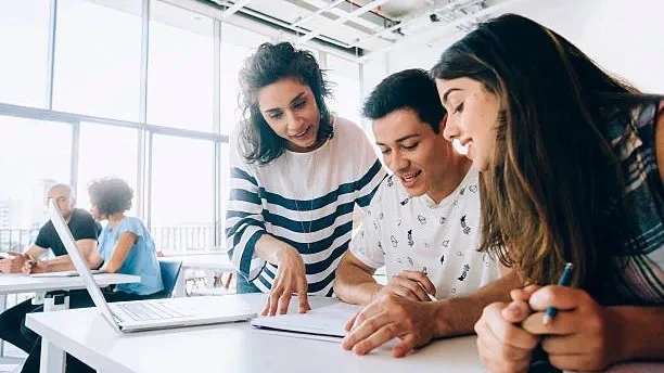 High school students collaborating with a mentor during a RISE Research summer program, working on STEM or humanities projects in a bright classroom setting.