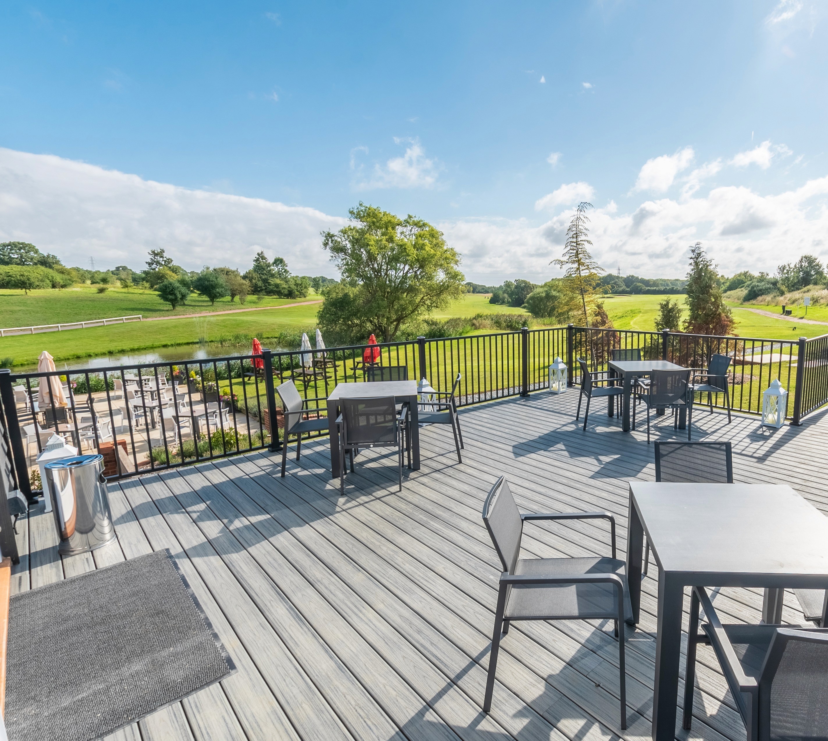 Outdoor deck with tables and chairs overlooking a golf course, under a blue sky with scattered clouds.