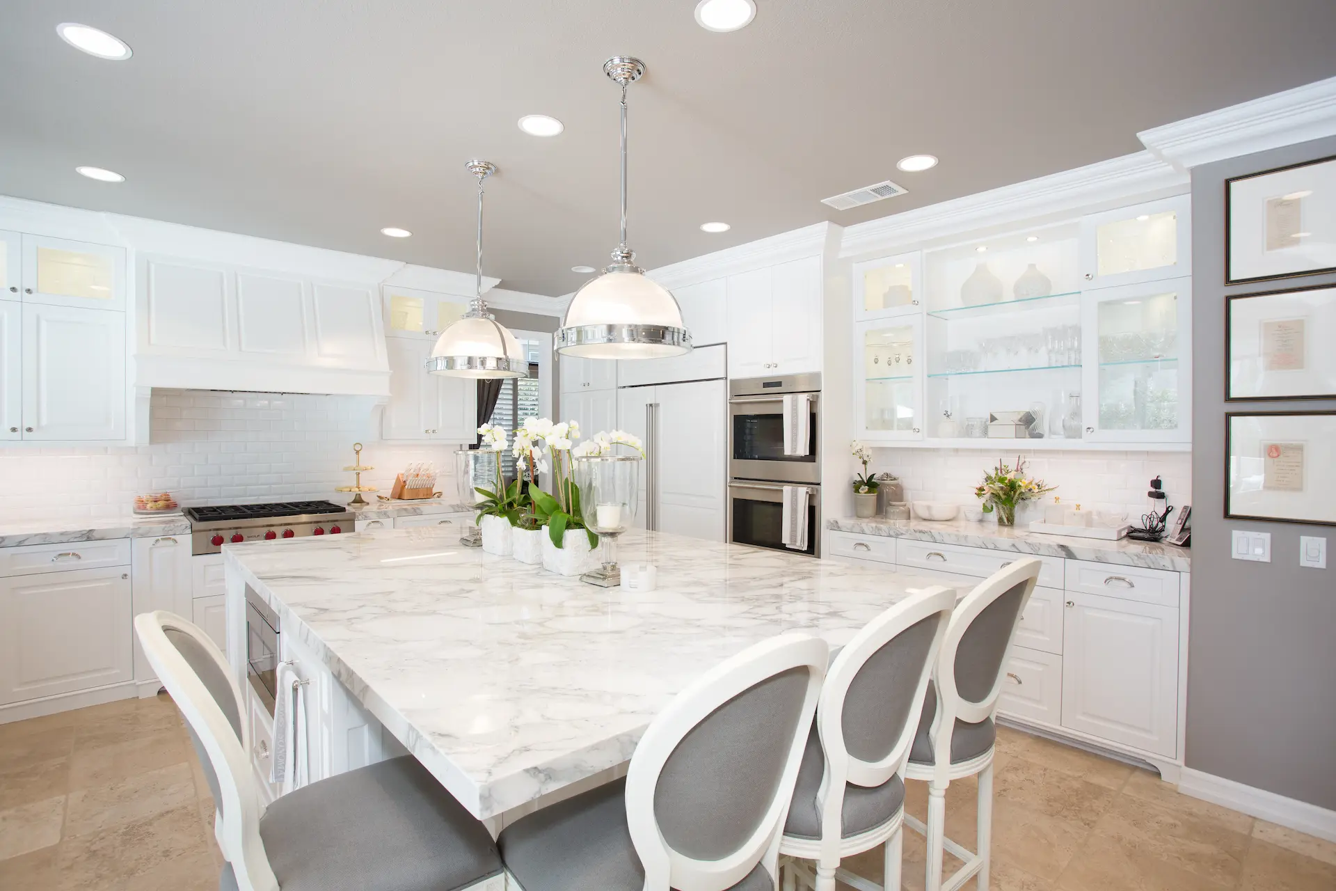 'Newport Beach Remodel' kitchen with a large marble island, white chairs, and elegant silver pendant lights.