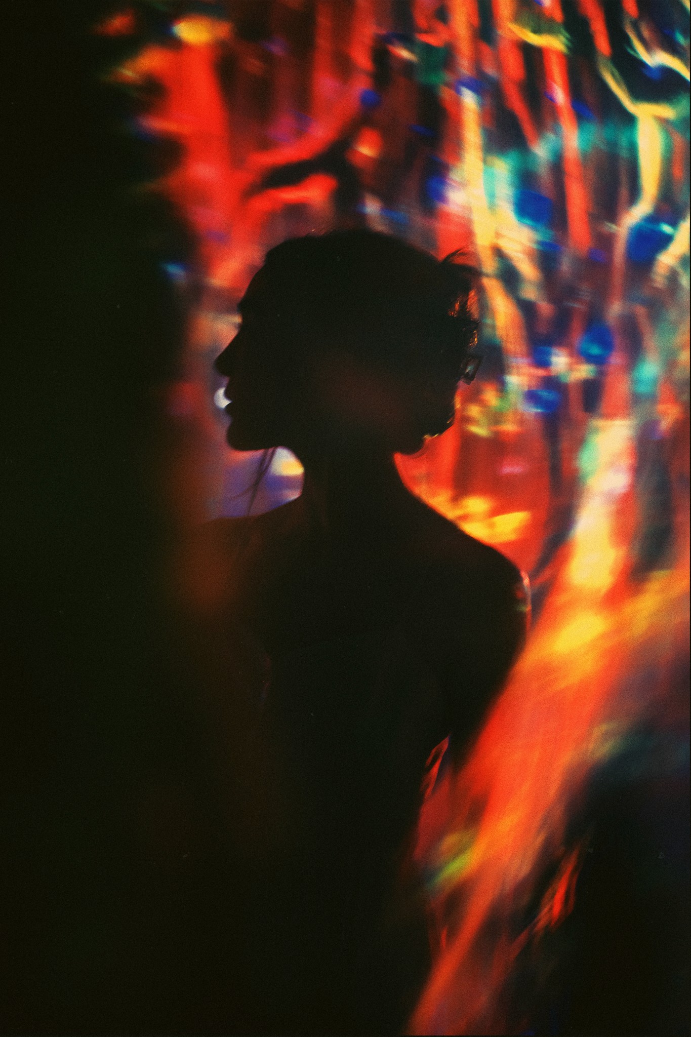 A silhouetted person stands against a vibrant, colorful abstract background with swirling patterns of red, orange, and blue light.