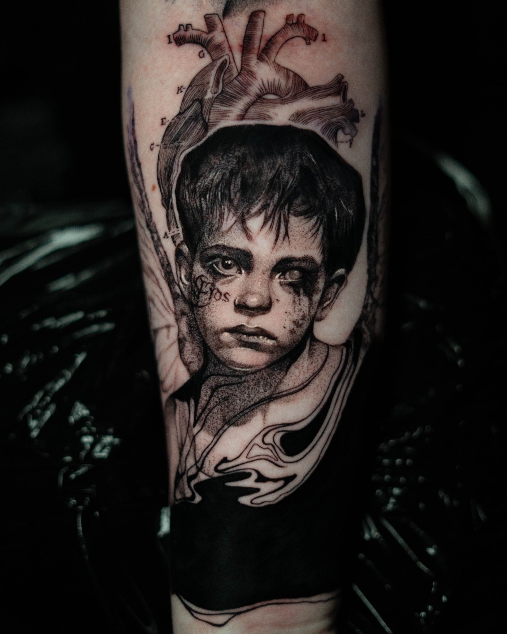Black and grey tattoo by Molly in Oxford and Boston, featuring anatomical heart and portrait of a child with “Eros” under eye.