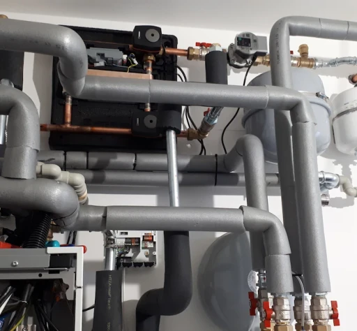 Detailní záběr na složitý vodovodní systém s trubkami, ventily a mechanickými součástmi. Zaměření na technické řešení a design.