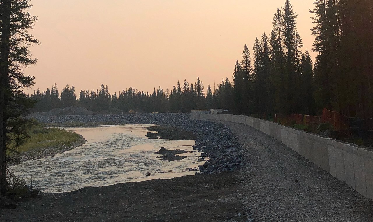 Completed riprap erosion protection along Elbow River with concrete wall at dusk near Bragg Creek