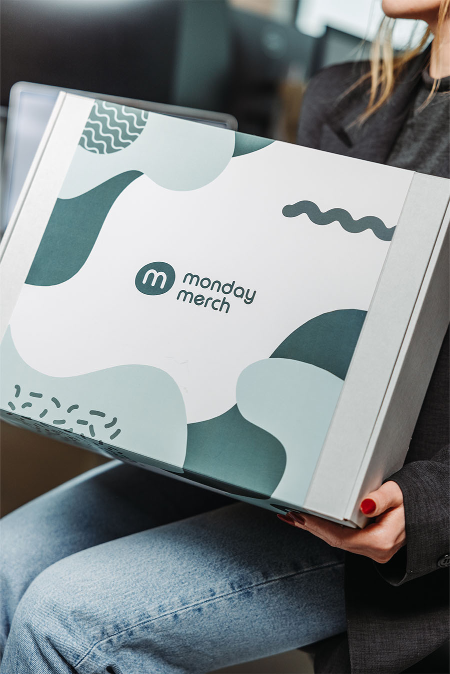Een persoon die een doos vasthoudt met het merk "Monday Merch"