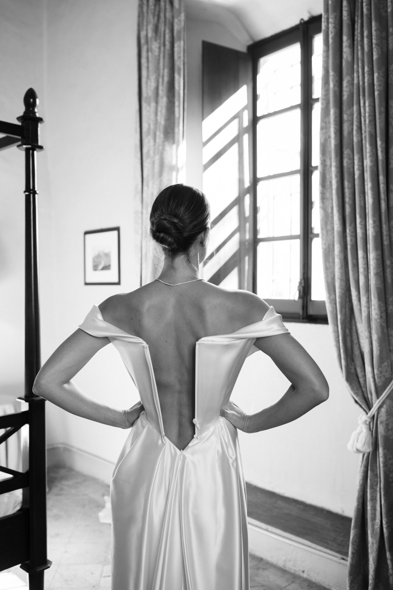 Sposa di spalle in abito bianco davanti alla finestra del Castello di Scipione, luce naturale sul dettaglio dello schiena