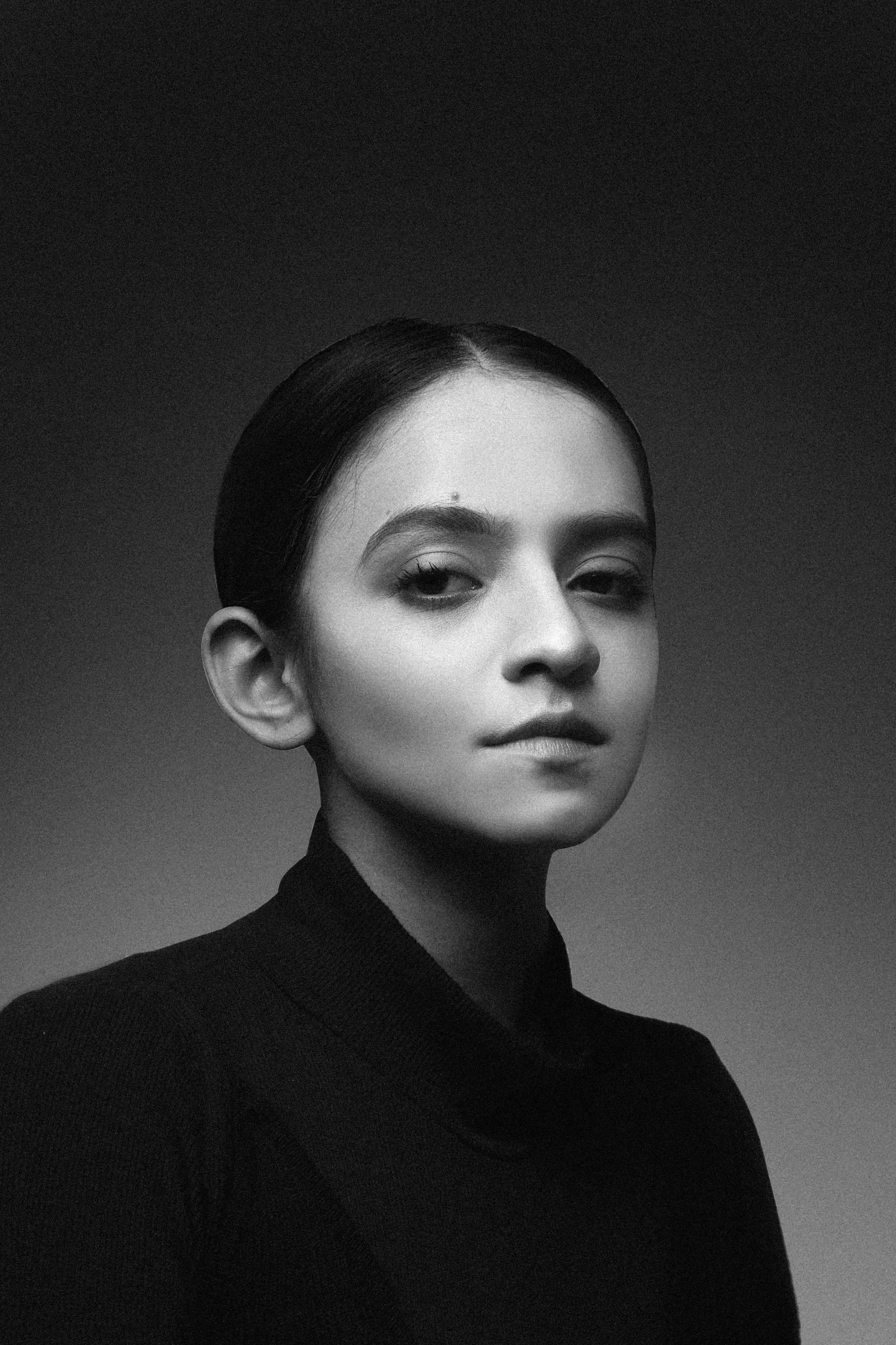 Black and white studio portrait of a woman with tied-back hair in a dark top