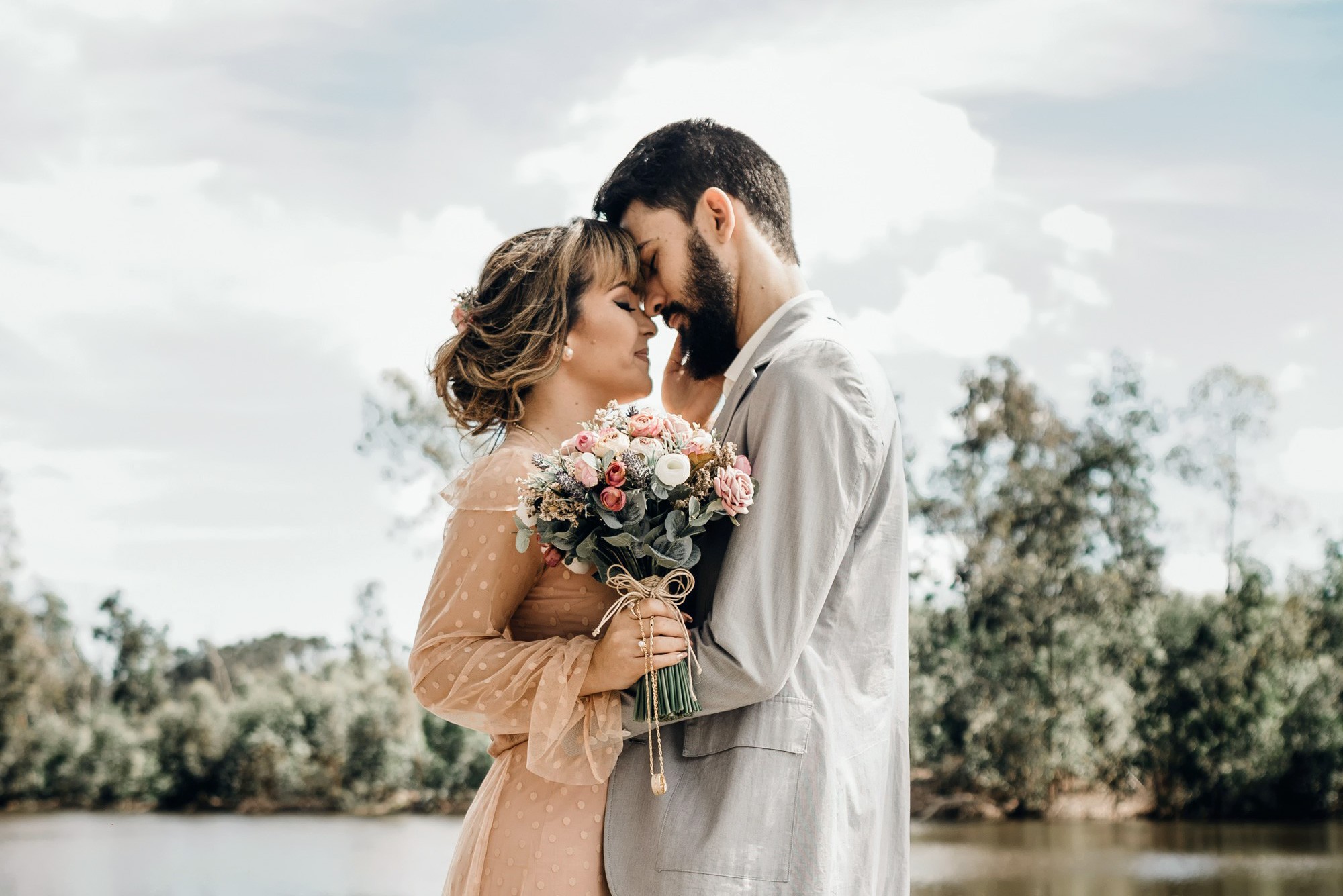A couple stands lovingly by a serene lakeside.