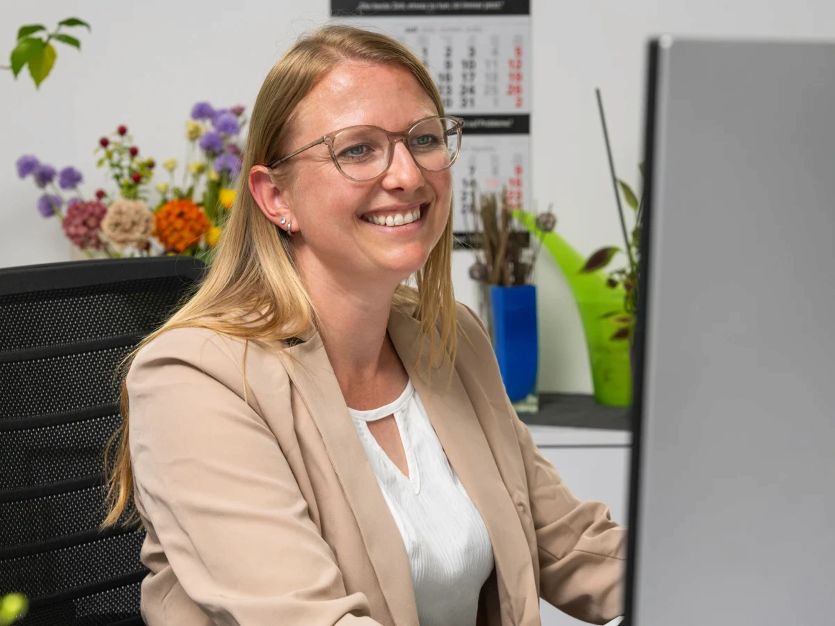 GJP-Mitarbeiterin arbeitet lächelnd an einem Bildschirm im Büro