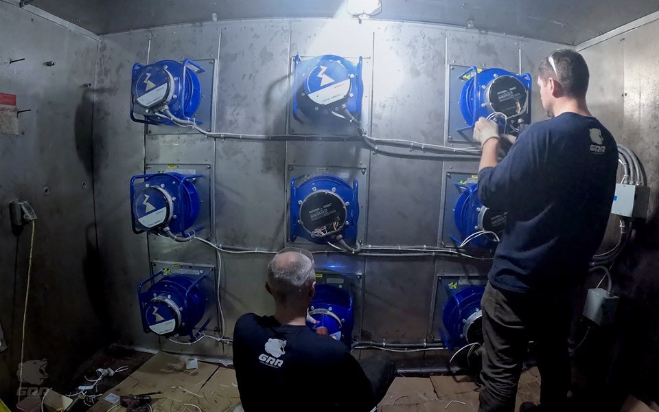 GRR Cooling Experts technicians installing and wiring a multi-fan EC fan array inside an air handling unit during a New York retrofit. The image shows several blue EC fan modules mounted in a grid, with technicians performing electrical and mechanical work in a confined AHU plenum.