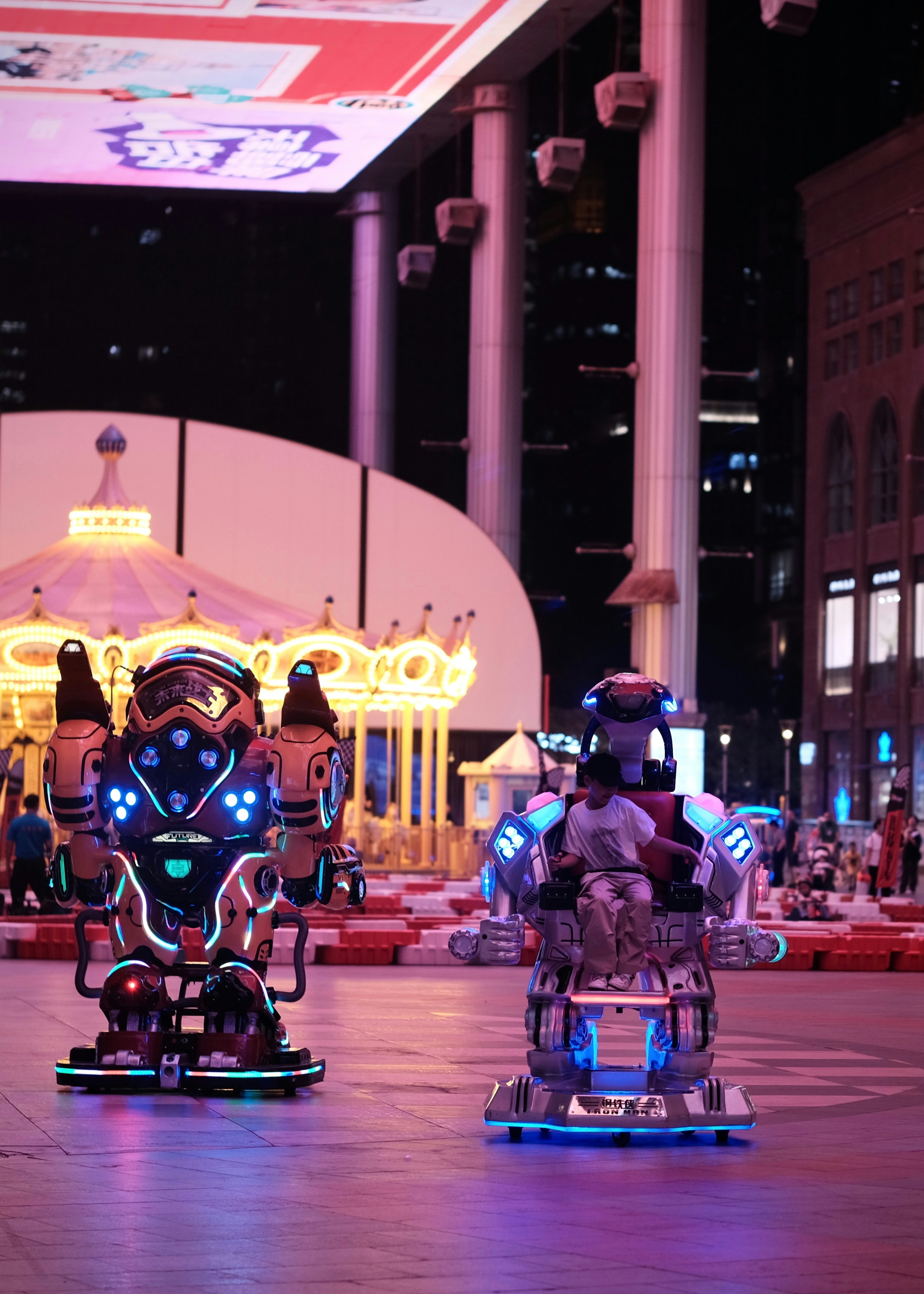 Two illuminated robots stand in a nighttime amusement park.
