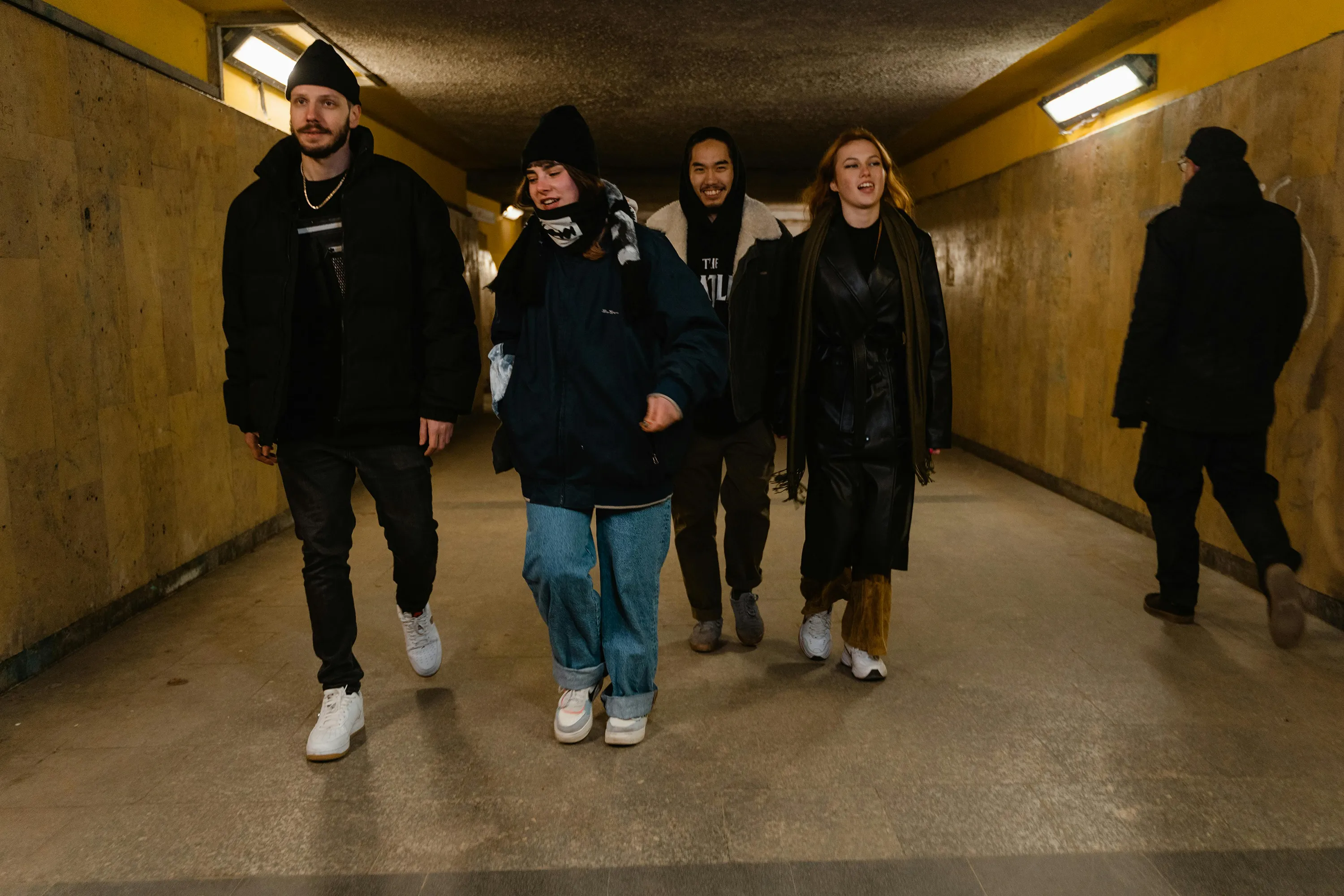 Four friends in winter streetwear laughing in an underpass