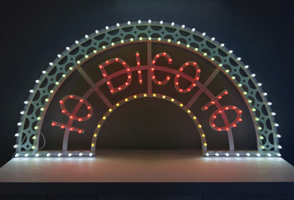 A colorful arch with the word "DISCO" lit up in bright red and white lights against a dark background.