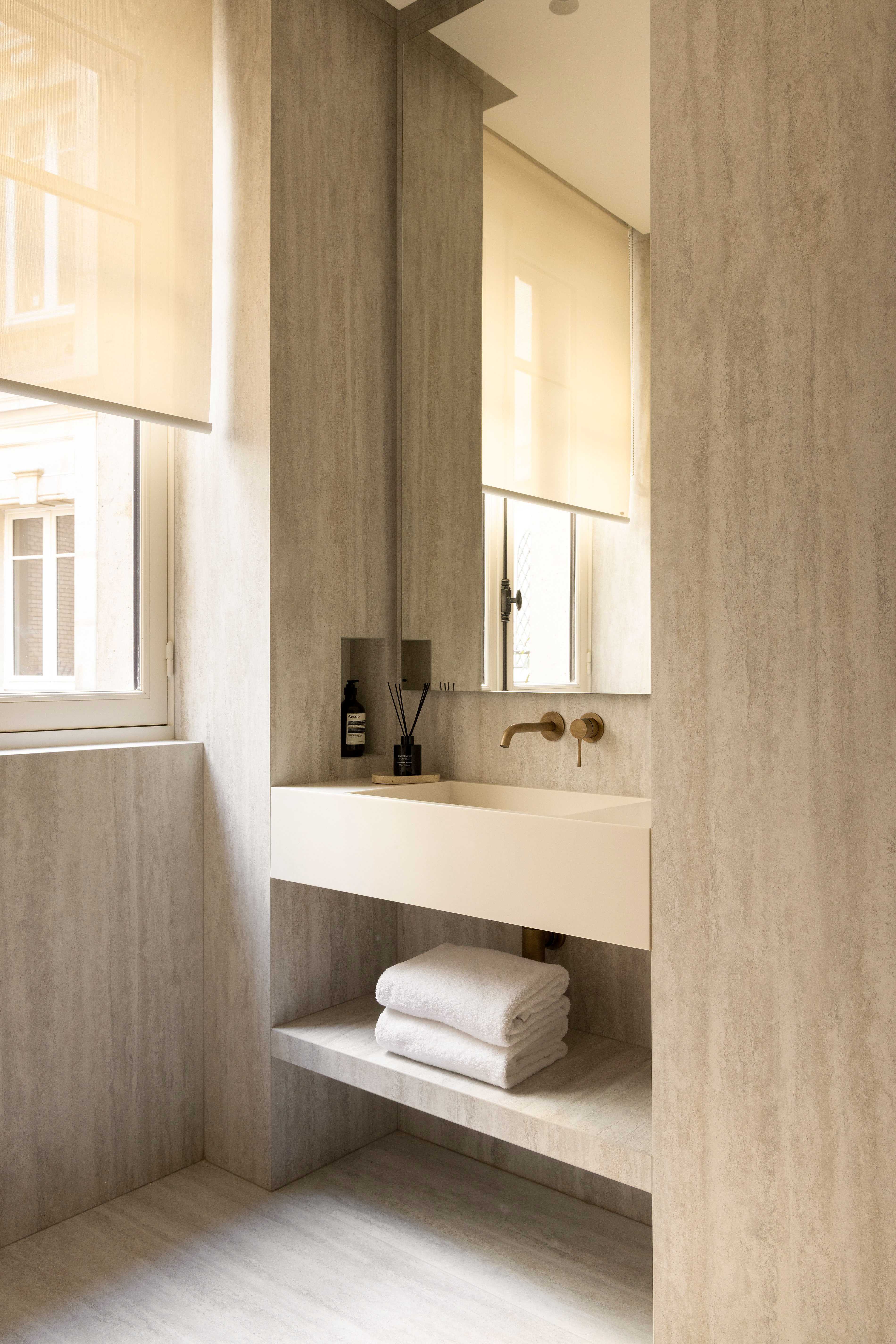 Vasque en pierre naturelle avec robinetterie dorée, miroir et serviettes sous fenêtre