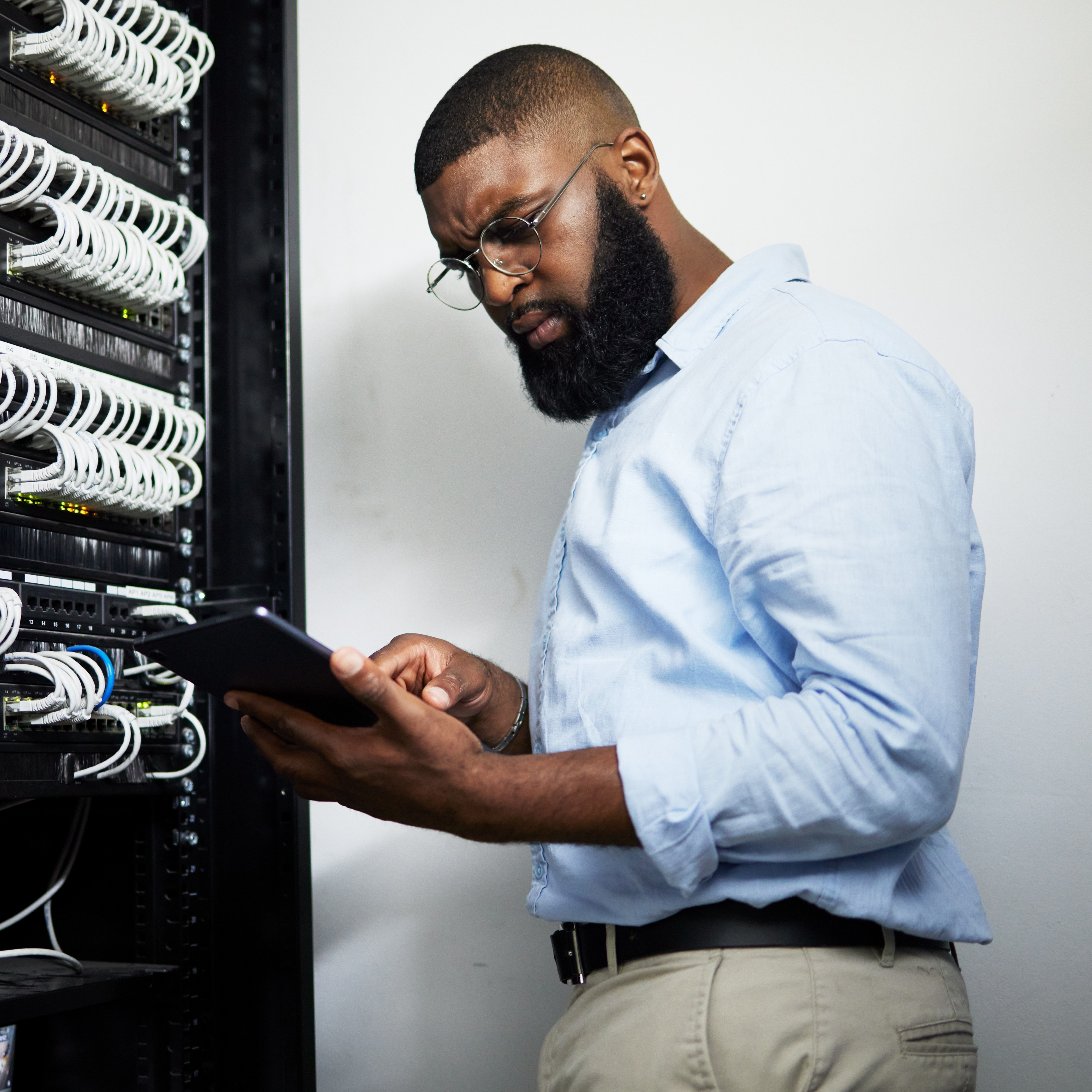 Serious IT professional using a tablet to configure servers in a data center, reflecting the integration of mobile technology in network management and maintenance.