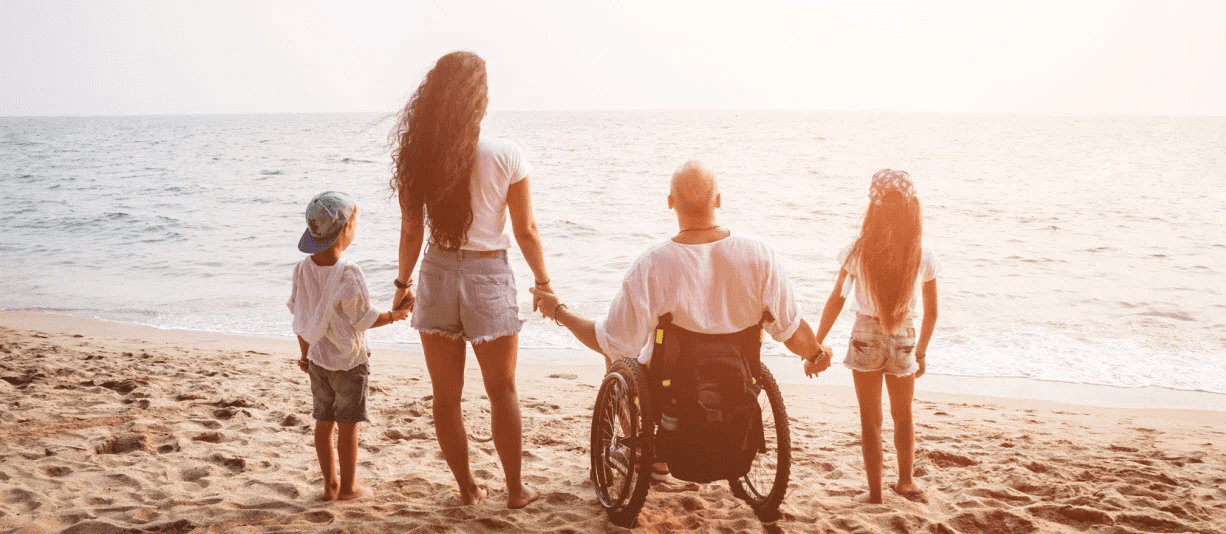 family at beach with father in wheelchair