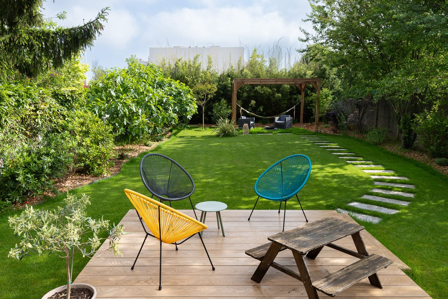 Un arbuste avec a son pied des fleurs et en fond une maison flou