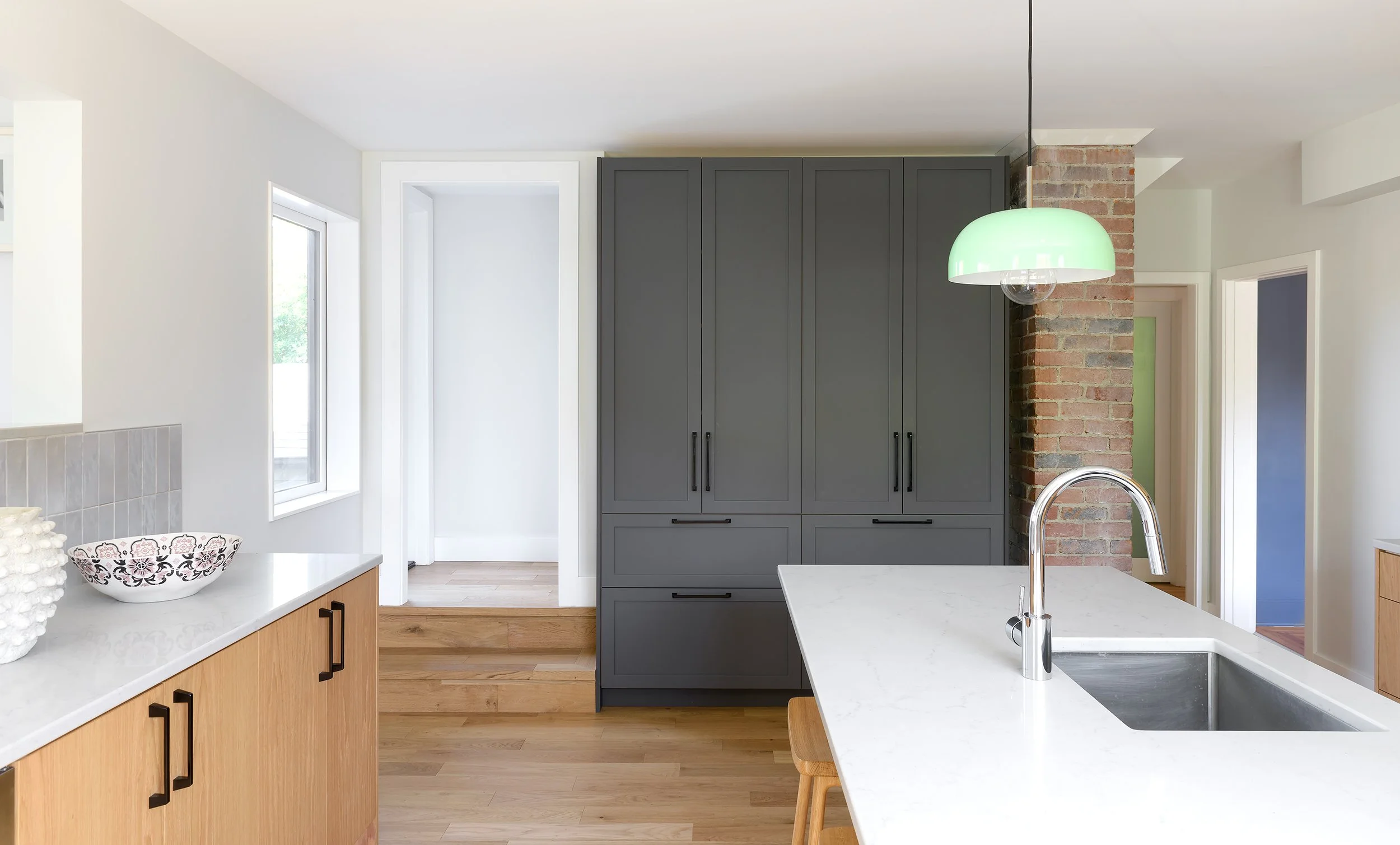 Modern two-story home with large glass windows, warmly lit interiors, and a balcony. Surrounded by trees and a manicured lawn at dusk. Cozy ambiance.