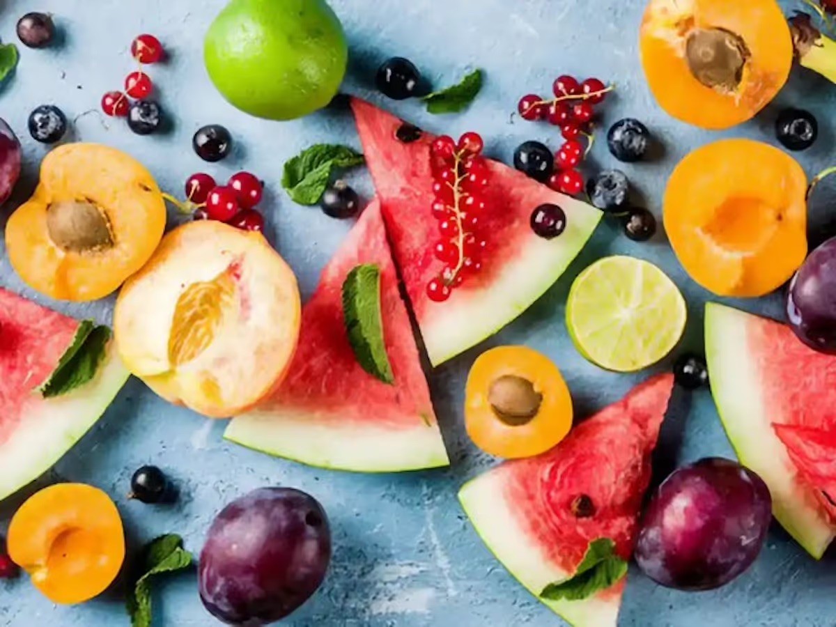 A colorful assortment of fresh fruit, including watermelon, apricots, grapes, and berries, arranged on a blue background.