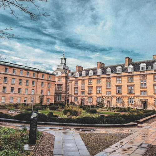 由砖石建成的建筑群,其中有一个中心庭院和步道,周围环绕着树篱。背景是阴天的天空。