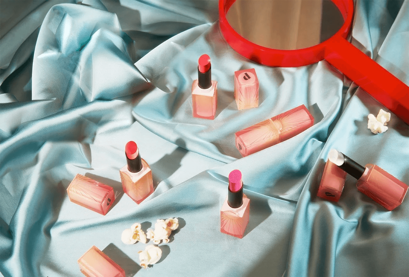Colorful Pley cosmetic products arranged on light blue satin with a red hand mirror