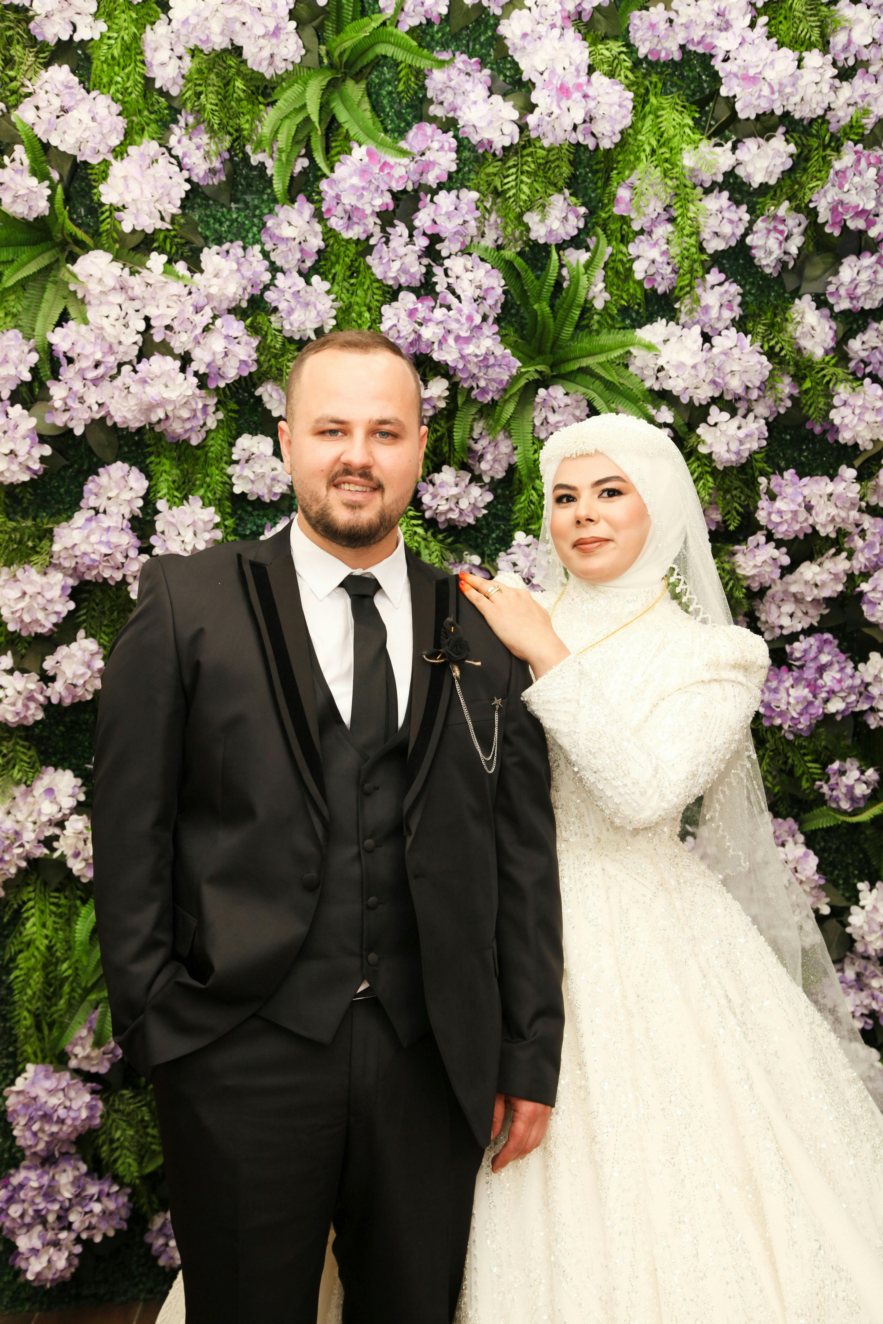 bride-and-groom-in-formal-attire-pose-before-lush-floral-wall,-exuding-elegance. - dilara-doğar (pexels)