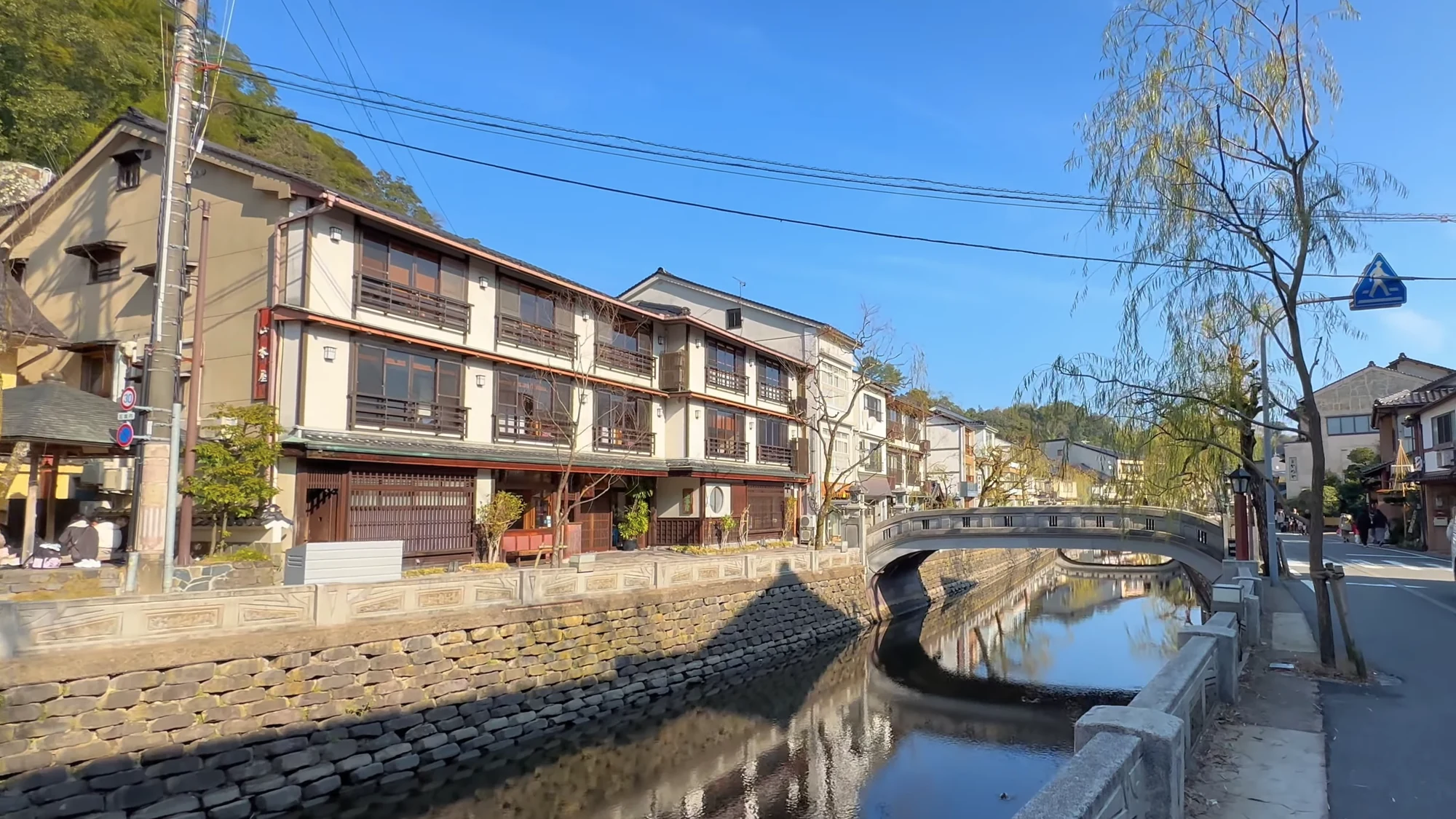 An arched stone bridge over the Kinosaki canal under a clear spring sky.