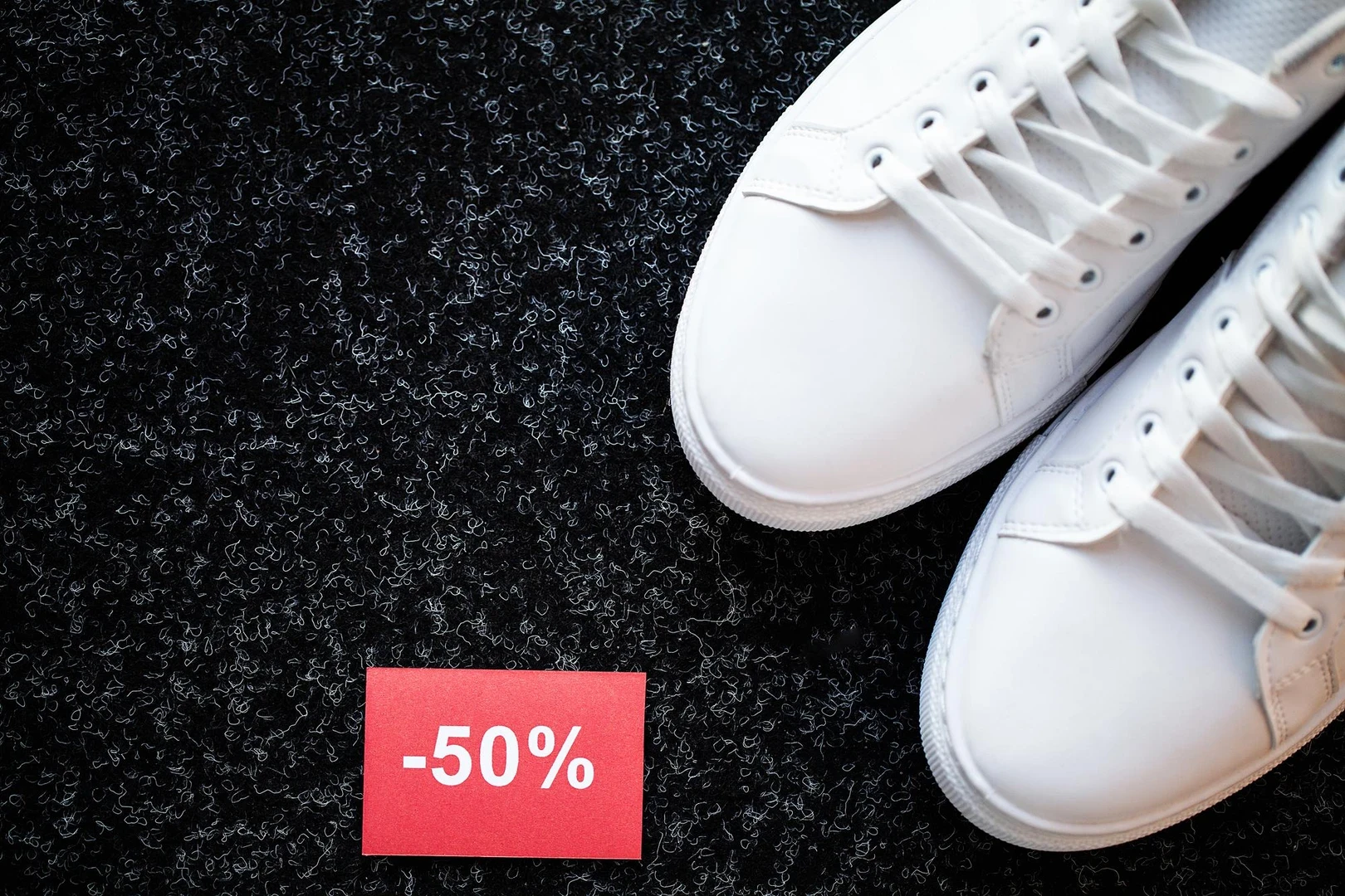Zapatillas blancas sobre fondo oscuro junto a una etiqueta de descuento