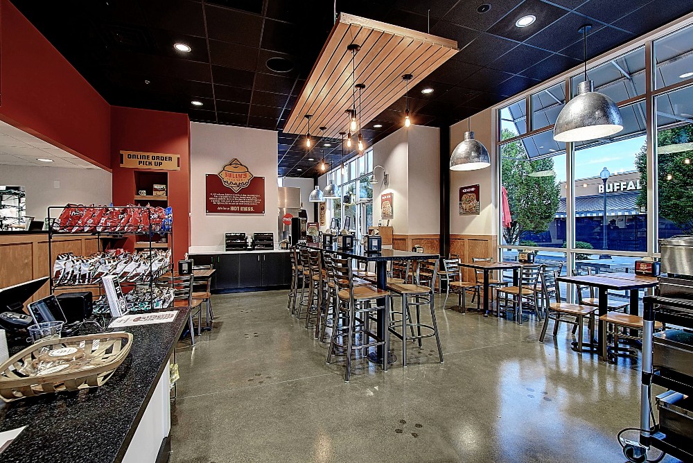 Modern restaurant interior with seating, large windows, and warm lighting, featuring a casual dining atmosphere.