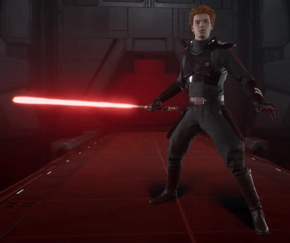 Cal Kestis wearing a black Inquisitor outfit and holding a red lightsaber to the side. He is standing on a grey Imperial looking walkway.