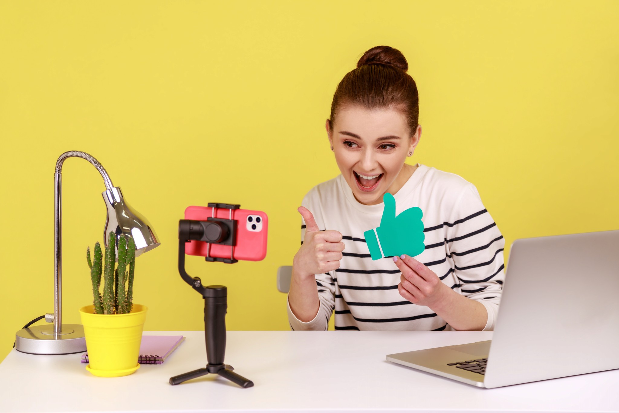 A woman stands holding a camera in one hand and a laptop in the other, ready to capture moments and ideas.