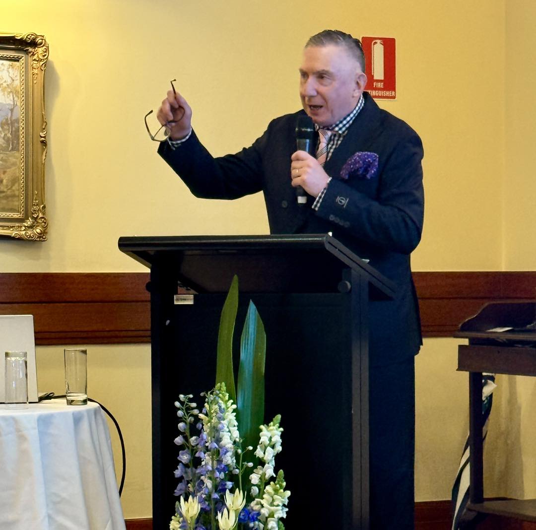 A person with red hair and a neutral expression wears a burnt orange vest over a beige shirt, accented by a brown scarf. The tone is calm and poised.