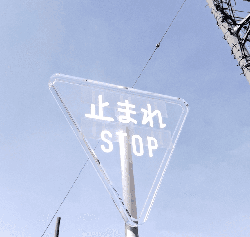 Transparent Japanese stop sign photographed against a blue sky.