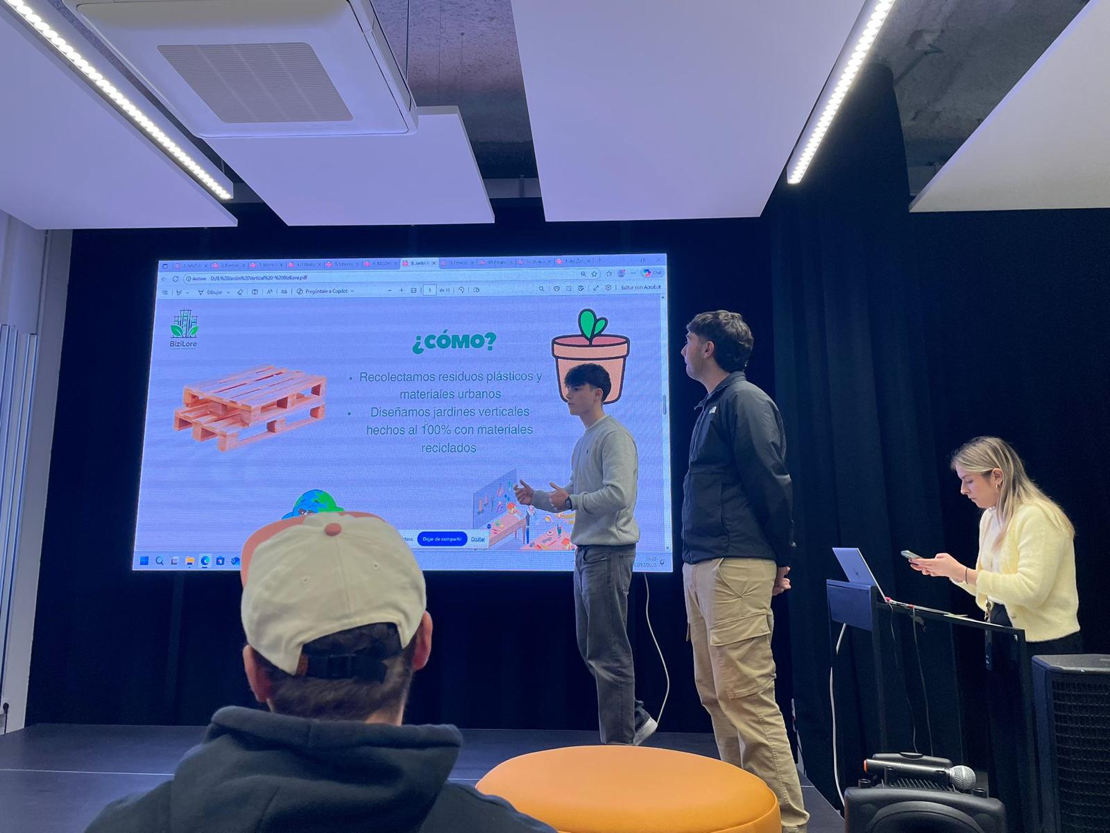 A smiling woman with her arms crossed, standing against a dark green background. She has long, dark hair.