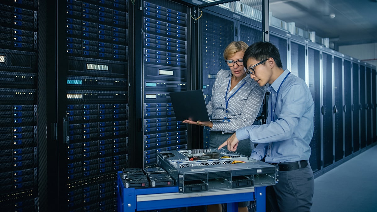Two professionals work together in a data center, examining equipment and servers.
