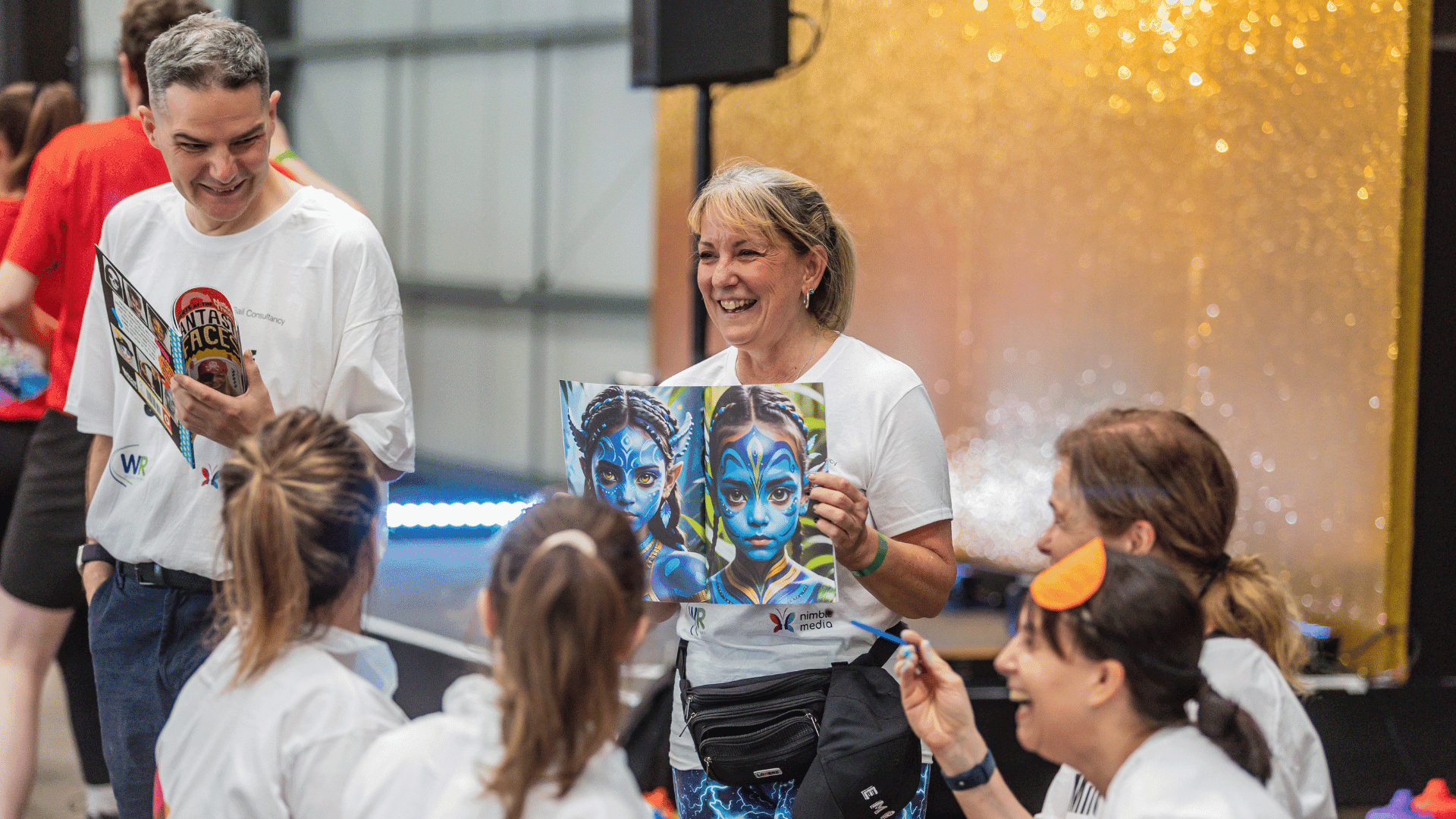 Outdoor team-building event with participants wearing matching blue shirts, taking part in inflatable obstacle courses and games, smiling and cheering, with the words 'ENTER A TEAM' in large bold white and green text across the image.
