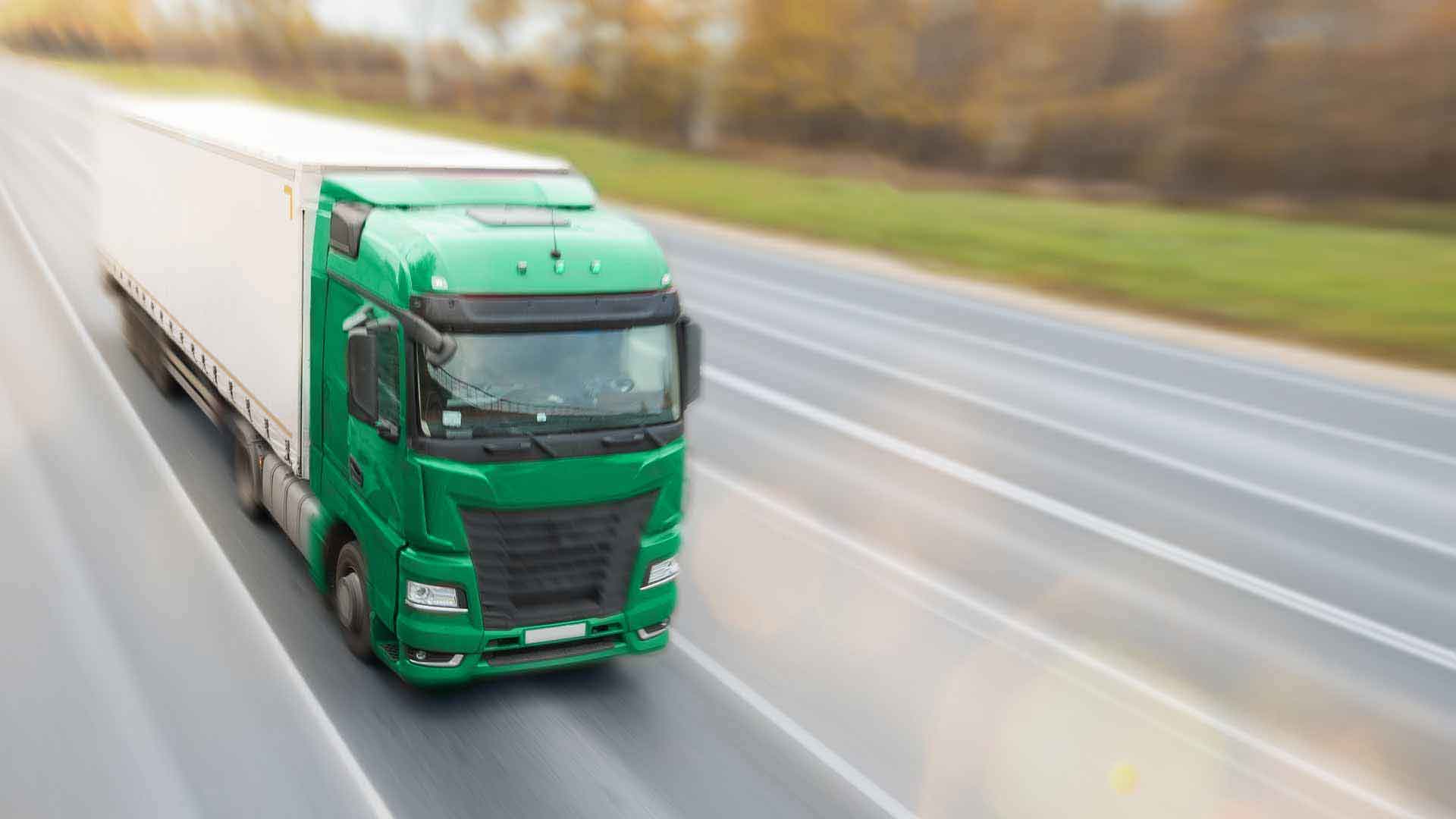 Автомобільні перевезення товарів, зелена вантажівка рухається автомагістраллю