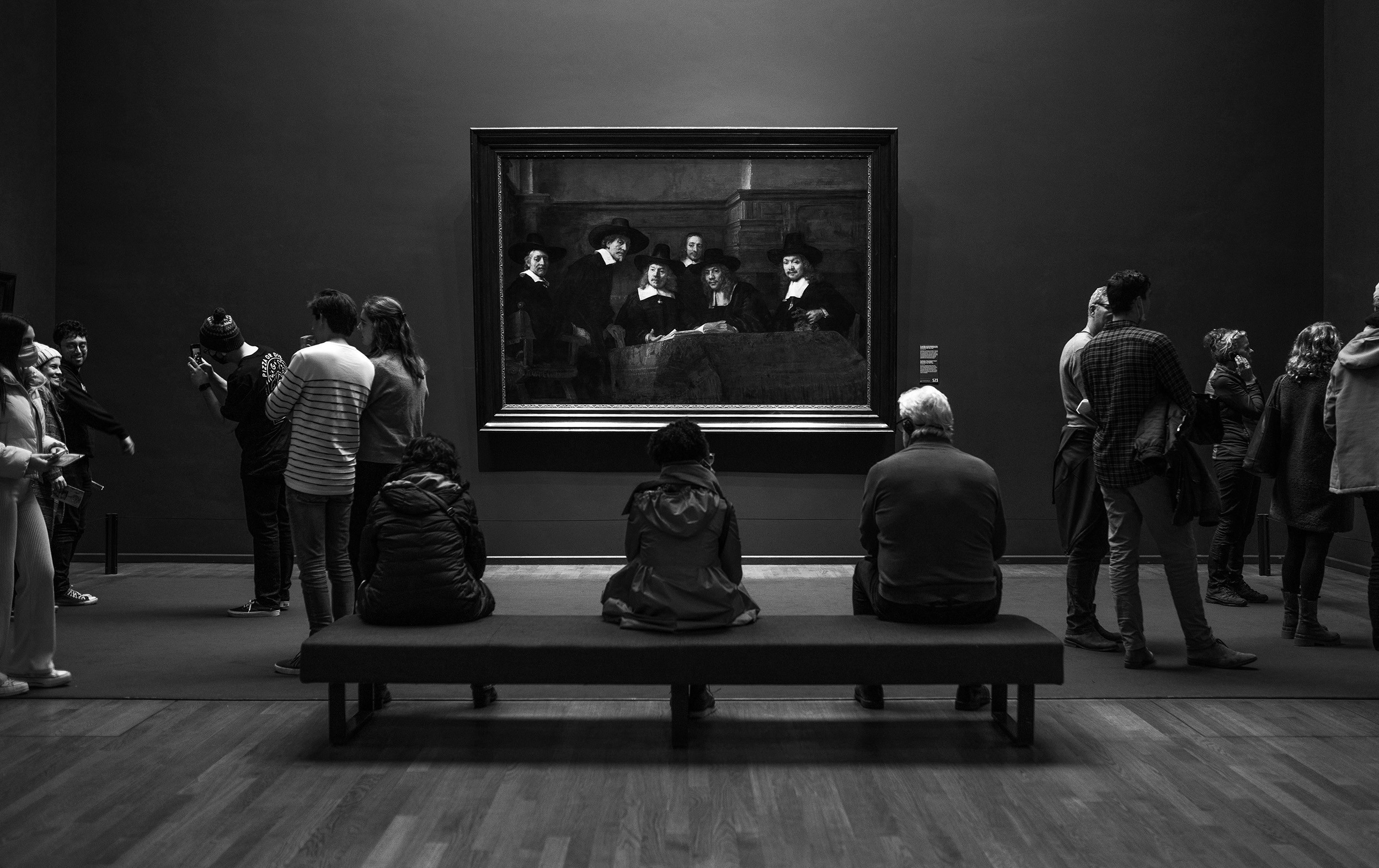 A dark museum hall with people viewing a Rembrandt painting