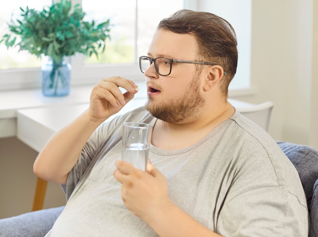 overweight man taking FDA-approved weight loss pills with a glass of water