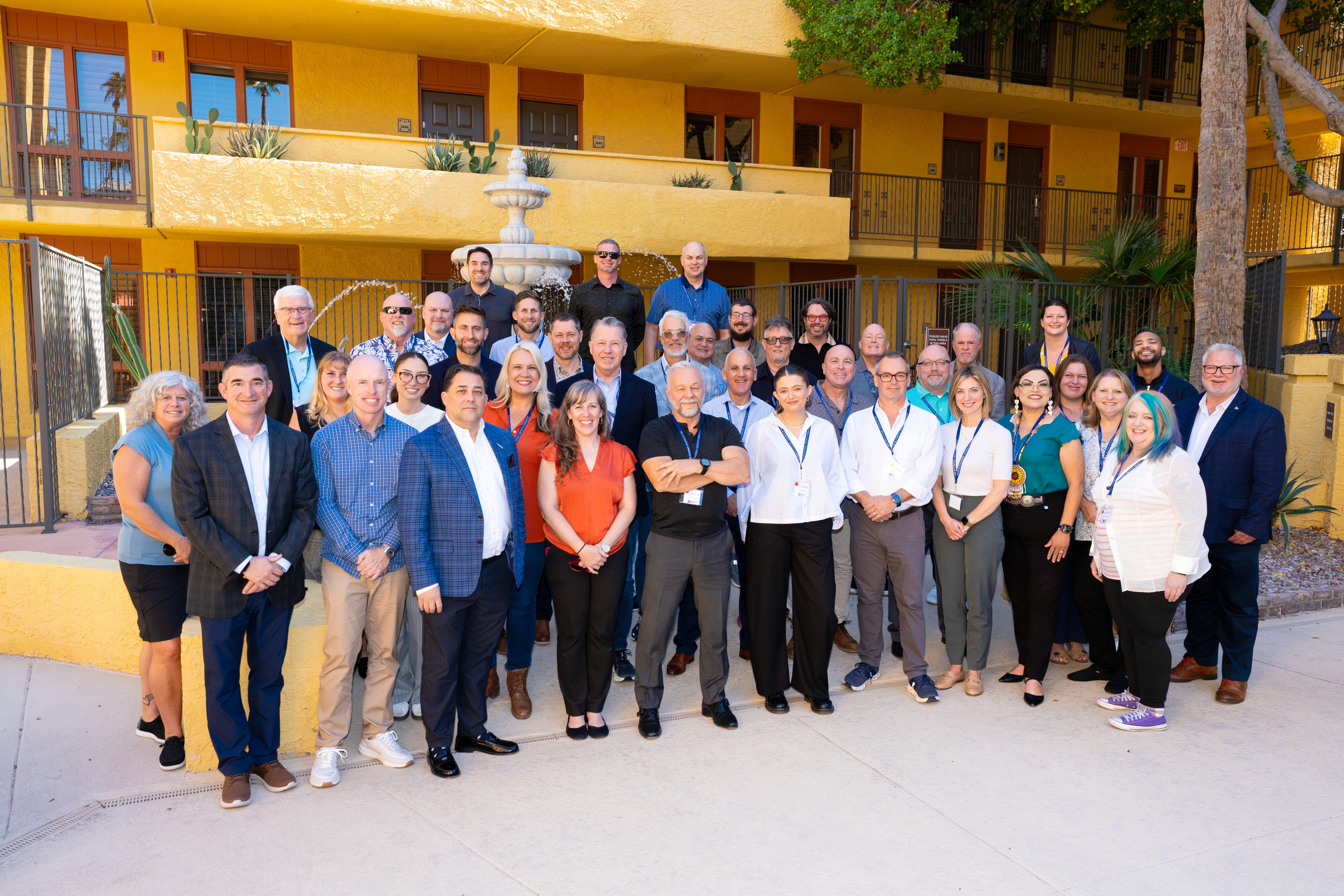 A father carries his daughter on his shoulders as she reaches into an open car trunk. They're by a car and some houses.