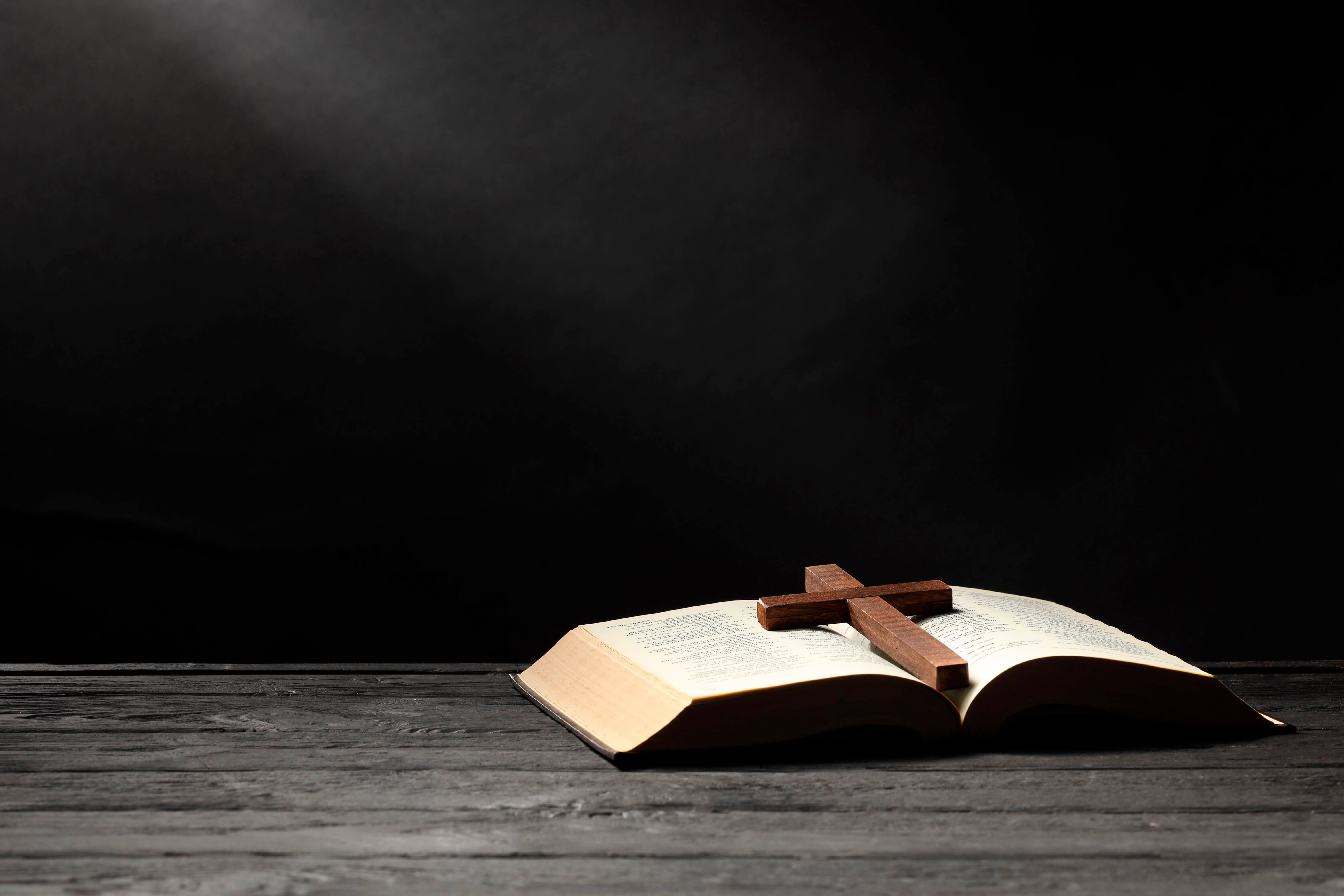 open bible sitting on table with christian cross on top