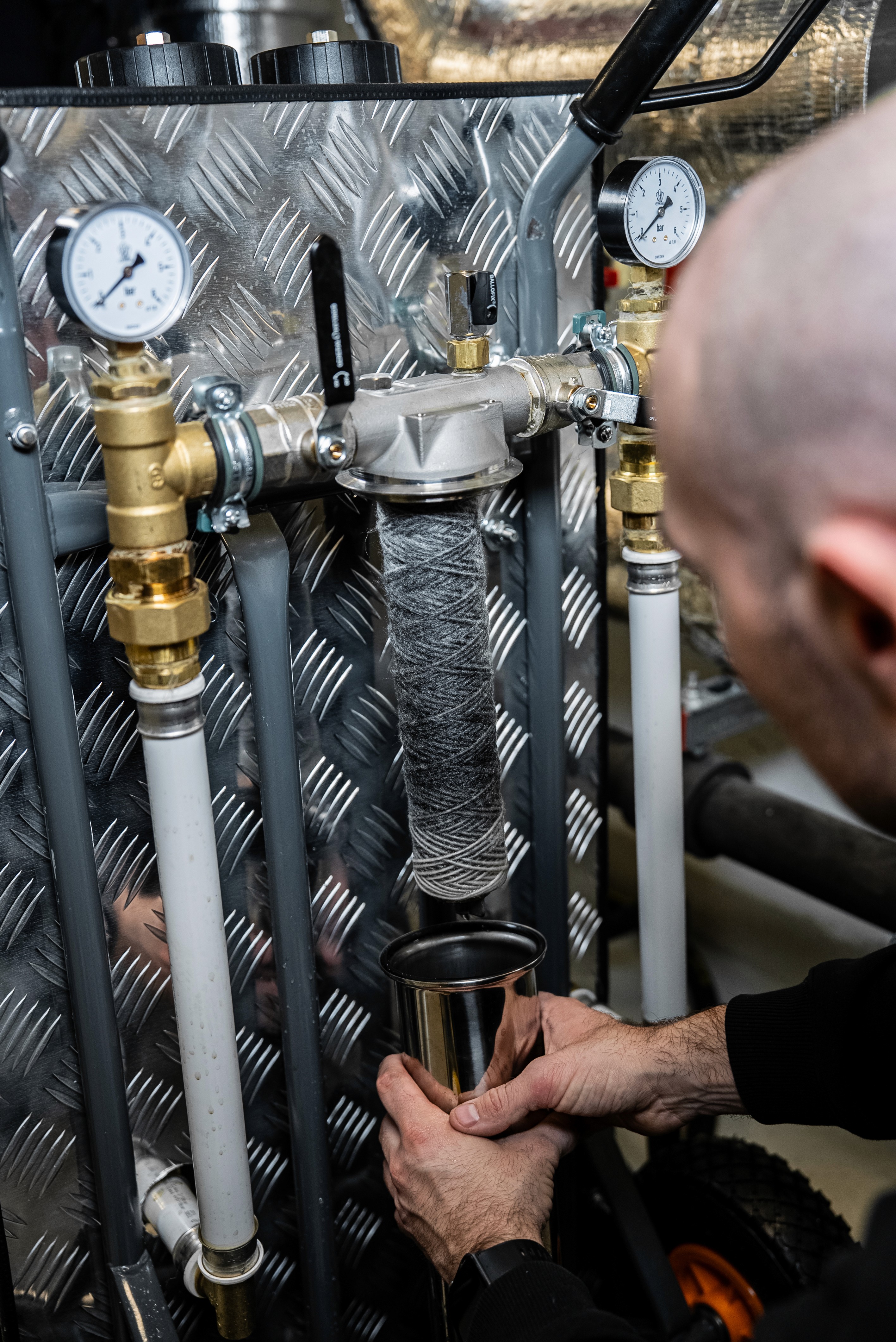 Young person wearing a bandana and plaid shirt holding a silver laptop next to a wooden table with tools.
