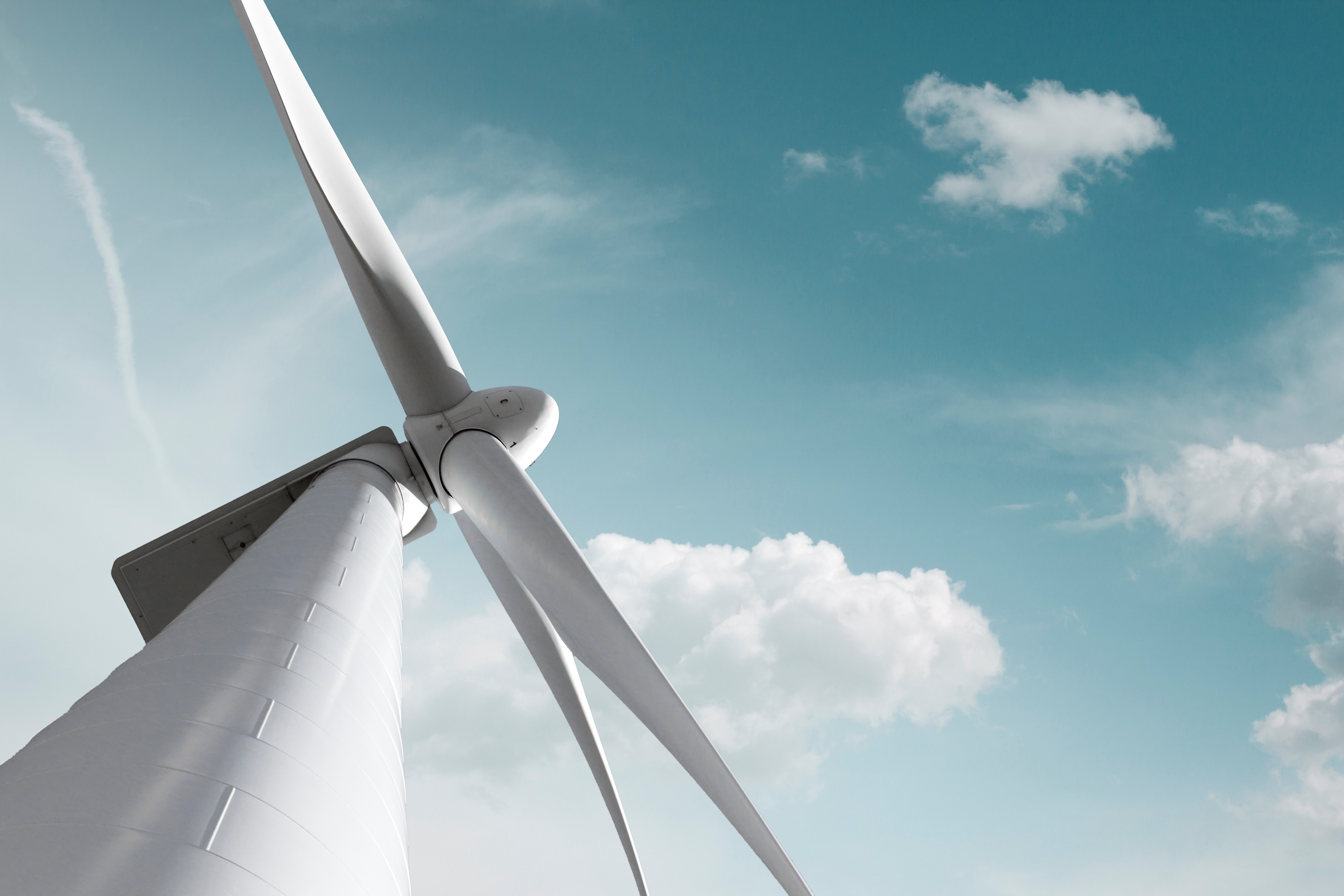 Windkraftanlage vor blauem Himmel als Symbol für wetterabhängige Stromerzeugung und volatile Strompreise.