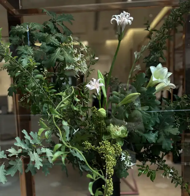 Arreglo floral contemporáneo con follaje verde y lirios blancos para decoración natural y estética botánica moderna.