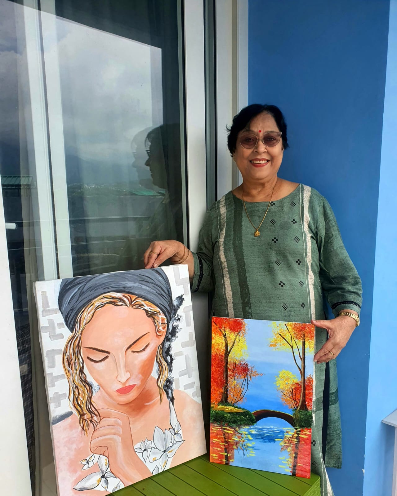 A person stands next to two paintings, one of a woman and one abstract, in the Creative Pod studio
